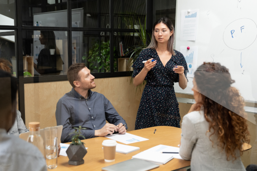 Woman leading conversation with team in front of white board with bar graph