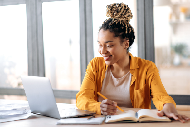 Woman working at laptop while taking notes