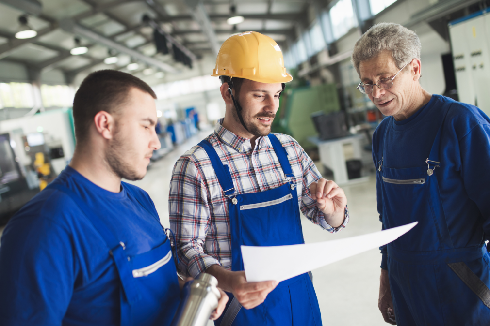 Three men of various ages wearing a hard hat in factory setting