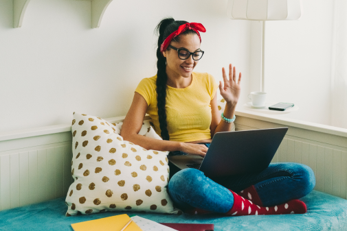 Student with a laptop waving to group on a virtual meeting